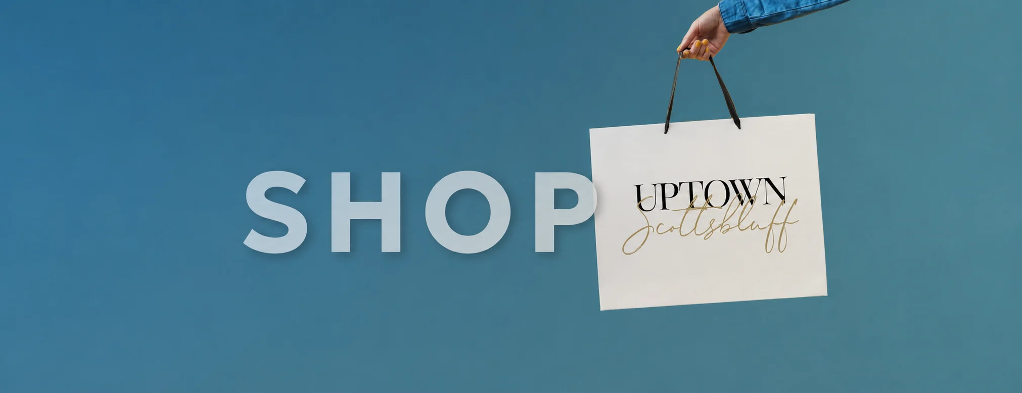 Shop Uptown Scottsbluff: a hand holding an Uptown Scottsbluff shopping bag