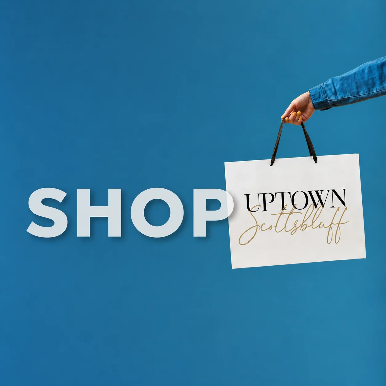Shop Uptown Scottsbluff: a hand holding an Uptown Scottsbluff shopping bag